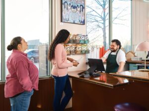 Restuarant staff member helping two customers at the counter, the kind of mement mystery shopping for franchises is built to catch.